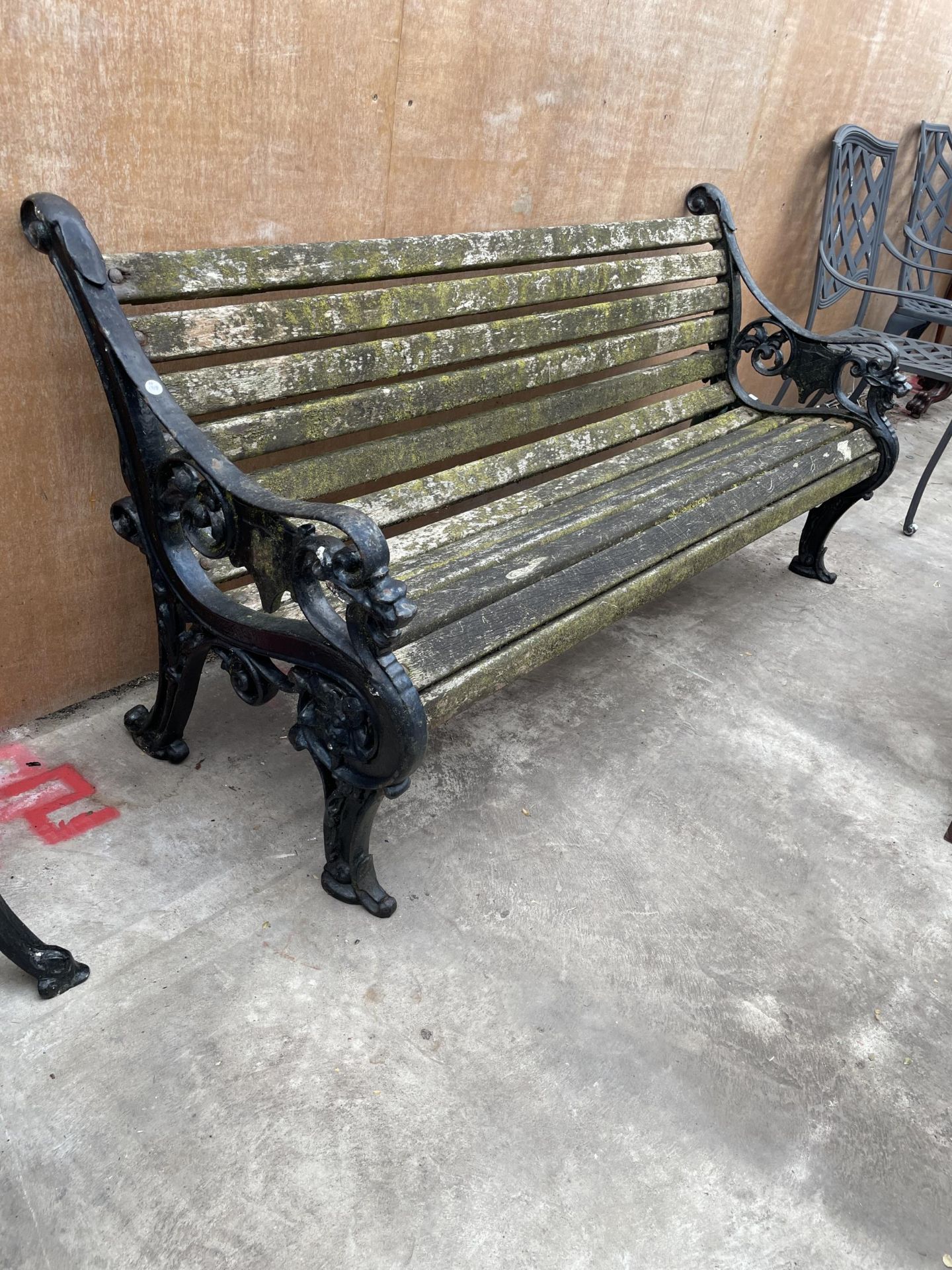 A HEAVY DUTY WOODEN SLATTED GARDEN BENCH WITH A PAIR OF HEAVILY DECORATED CAST IRON BENCH ENDS