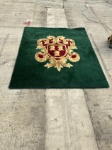 A GREEN AND RED PURE WOOL RUG WITH ARMORIAL CREST - INCLUDES SEVEN MATCHING CURTAIN TIE BACKS -
