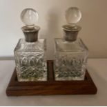 A PAIR OF ELIZABETH II 1986 & 1987 HALLMARKED BIRMINGHAM SILVER AND CUT GLASS DECANTERS ON WOODEN