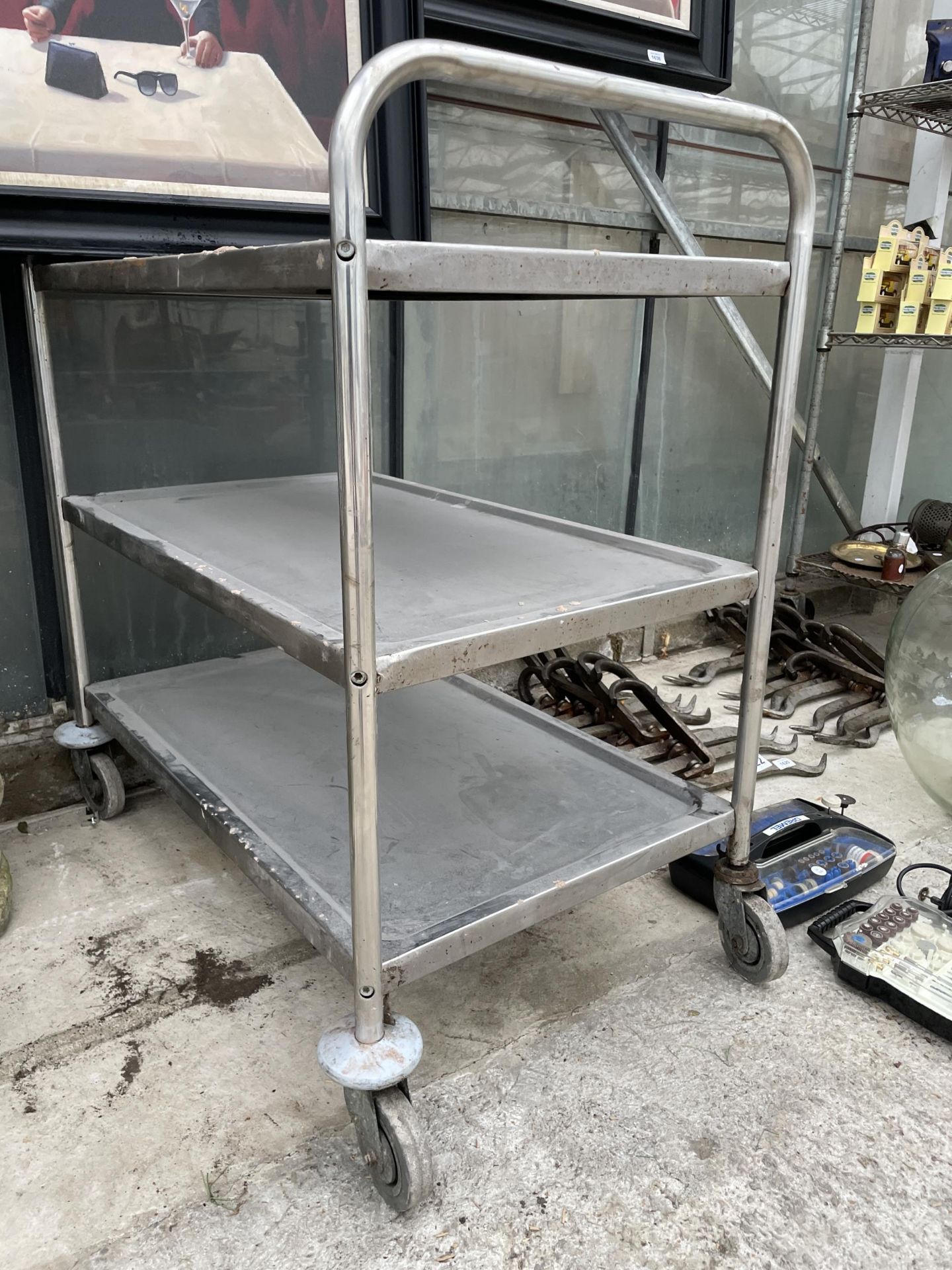 A THREE TIER STAINLESS STEEL FOUR WHEELED TROLLEY