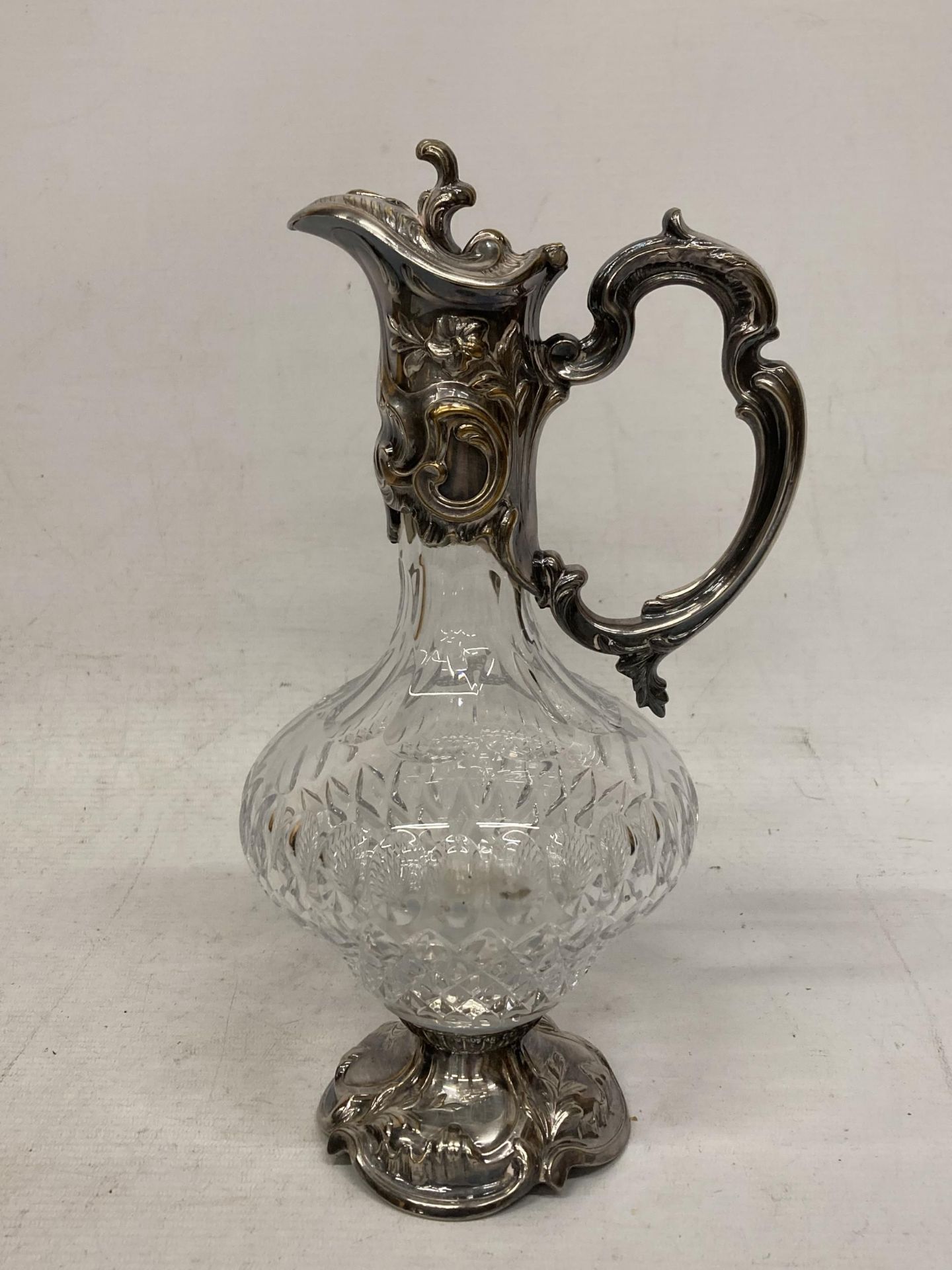 AN ORNATE SILVER PLATED AND CUT GLASS CLARET JUG