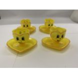 FOUR YELLOW PLASTIC EGGCUPS WITH HEART SHAPED SAUCERS AND FACES ON THE FRONT AND BACK