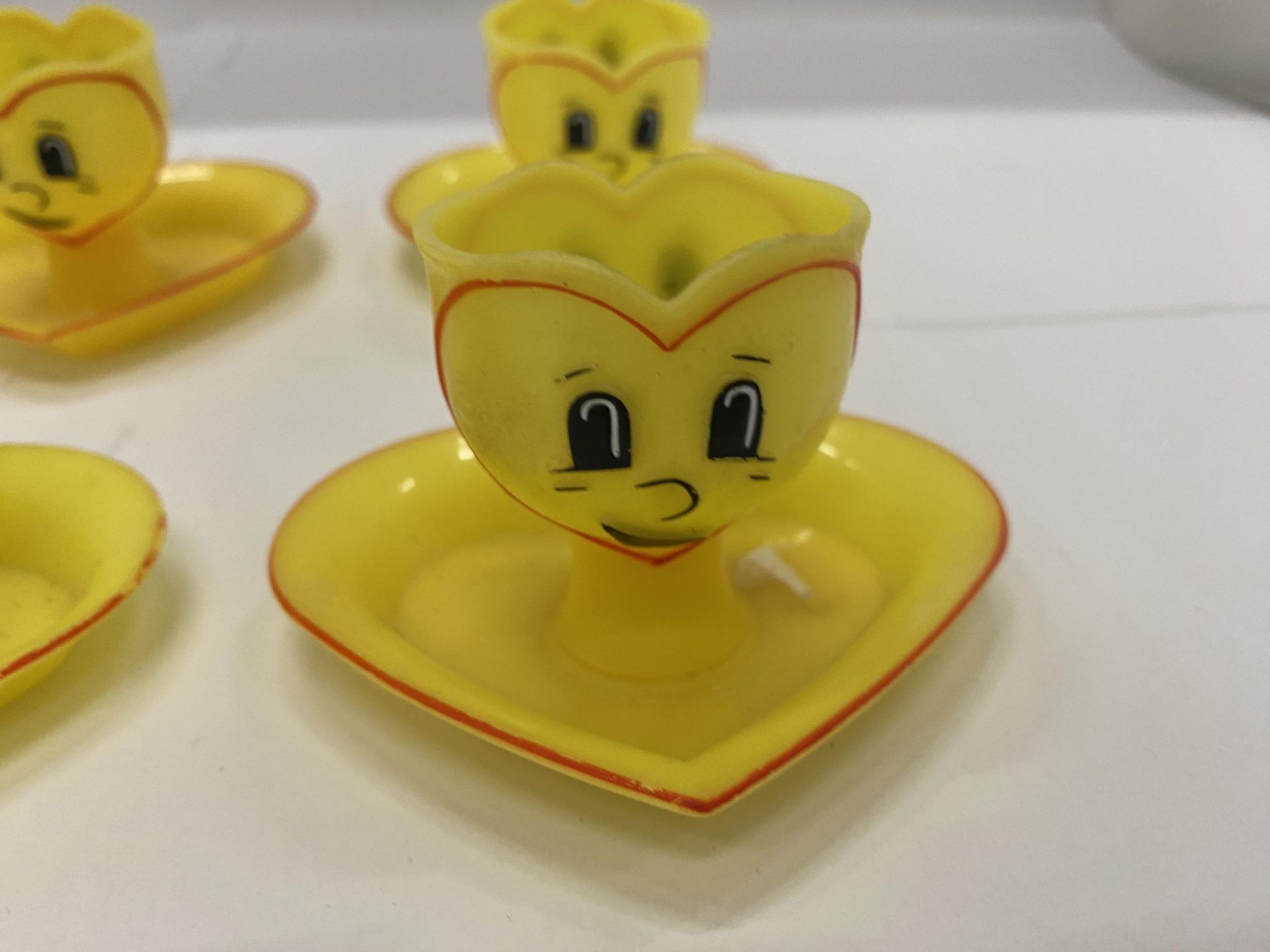 FOUR YELLOW PLASTIC EGGCUPS WITH HEART SHAPED SAUCERS AND FACES ON THE FRONT AND BACK - Image 2 of 3