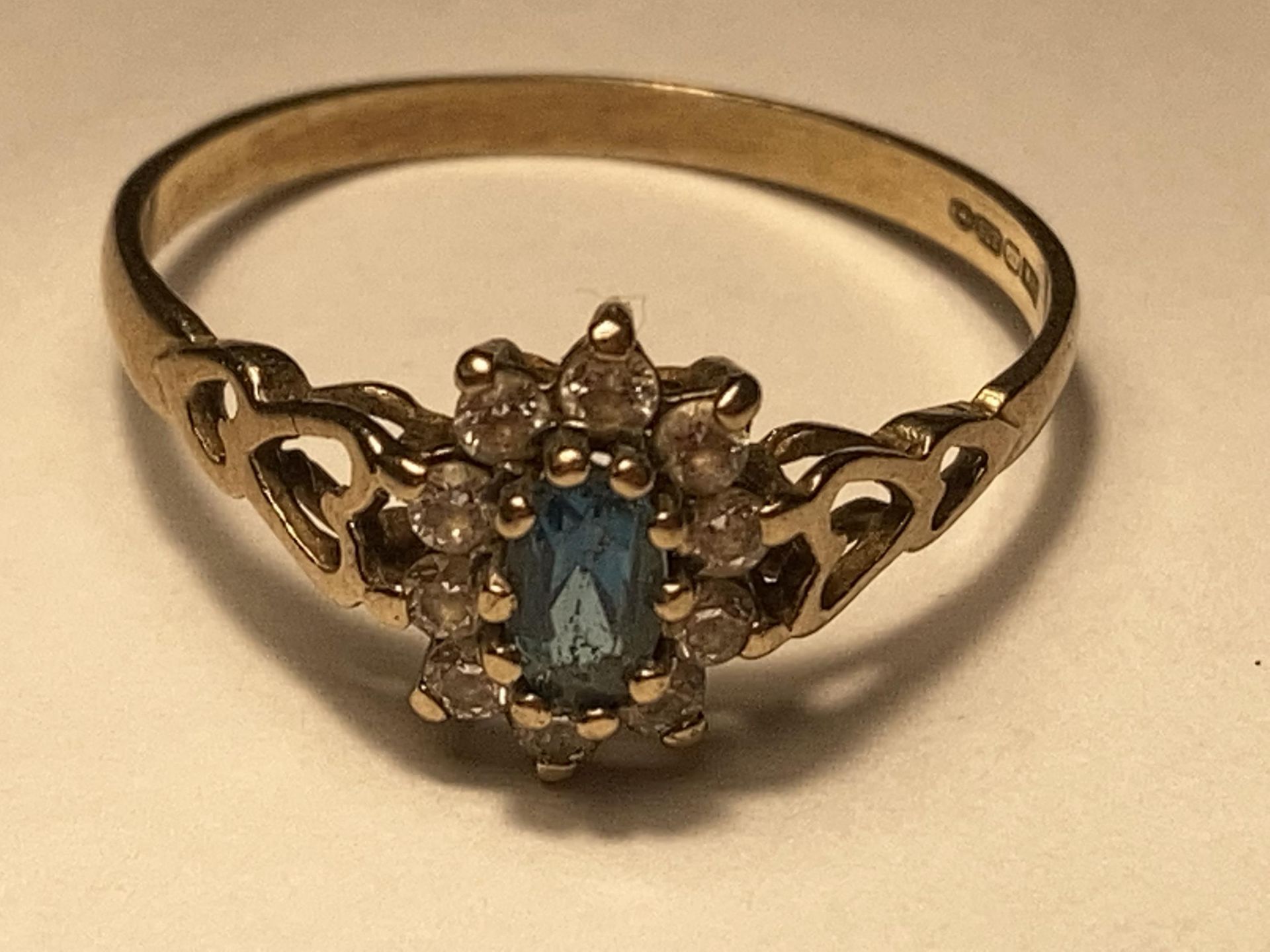 A 9 CARAT GOLD RING WITH A CENTRE BLUE TOPAZ STONE SURROUNDED BY CUBIC ZIRCONIAS SIZE O/P
