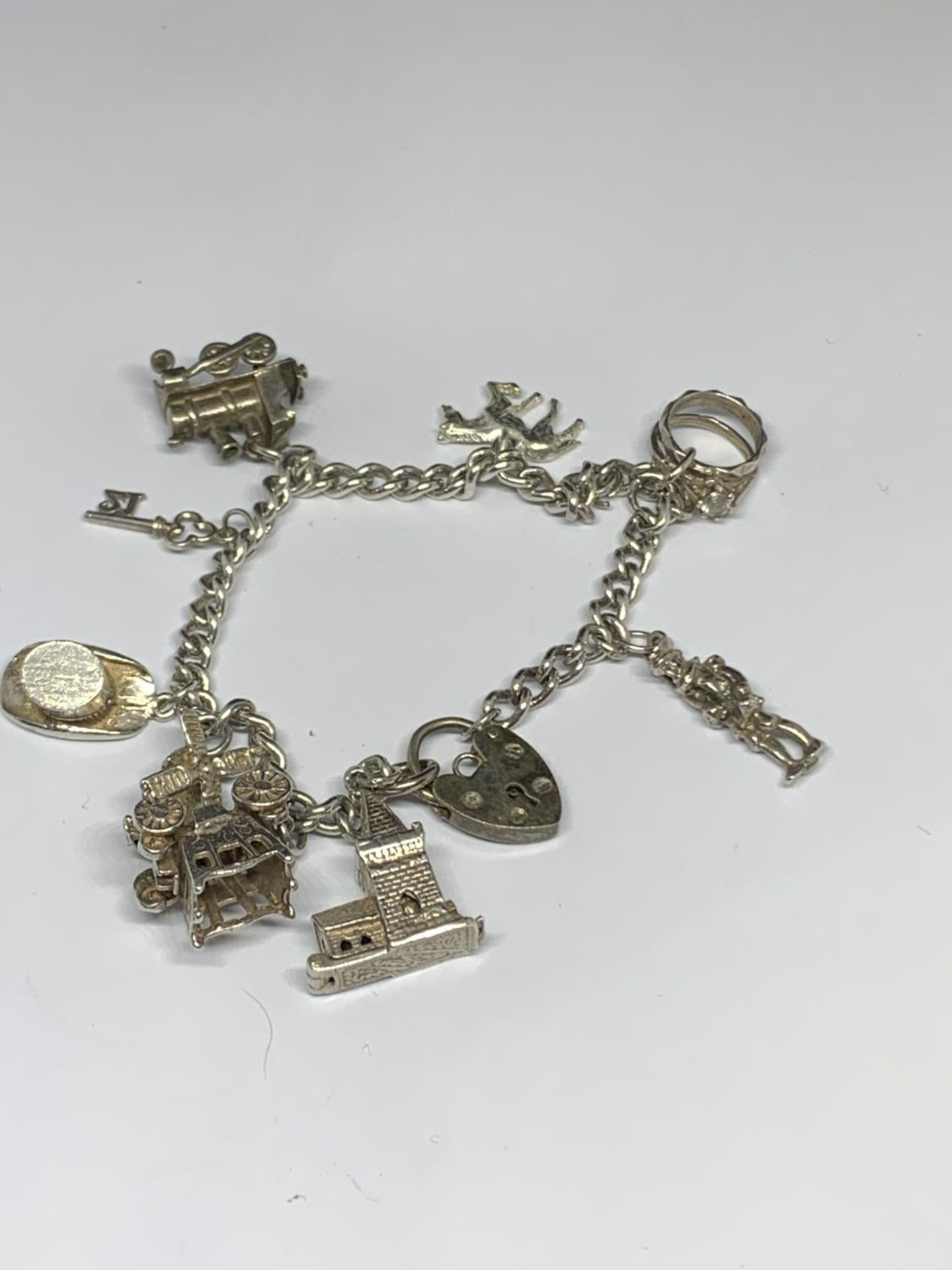 A SILVER CHARM BRACELET WITH NINE CHARMS AND A HEART PADLOCK