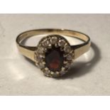 A 9 CARAT GOLD RING WITH CENTRE GARNET SURROUNDED BY CUBIC ZIRCONIAS SIZE R