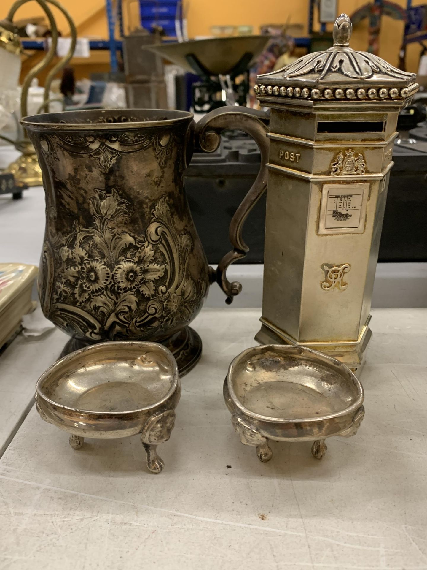 A SILVER PLATED ORNATELY DECORATED TANKARD, TWO SILVER PLATED OPEN SALTS AND A WHITE METAL POST