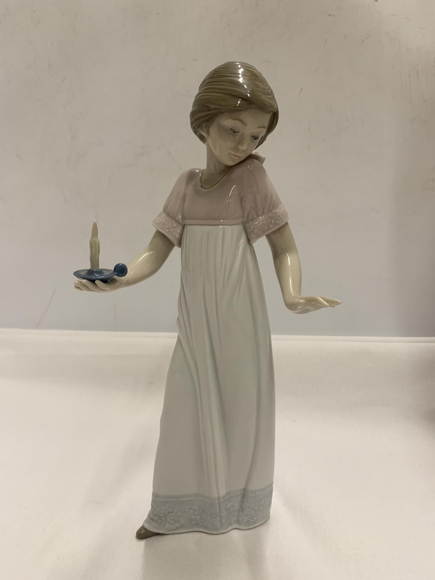 A NAO FIGURE OF A GIRL HOLDING A CANDLE