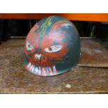 AN UNUSUAL LATE 20TH CENTURY U.S ARMY HELMET LINER WITH HAND PAINTED DECORATION OF A DEVIL FACE WITH