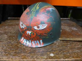 AN UNUSUAL LATE 20TH CENTURY U.S ARMY HELMET LINER WITH HAND PAINTED DECORATION OF A DEVIL FACE WITH