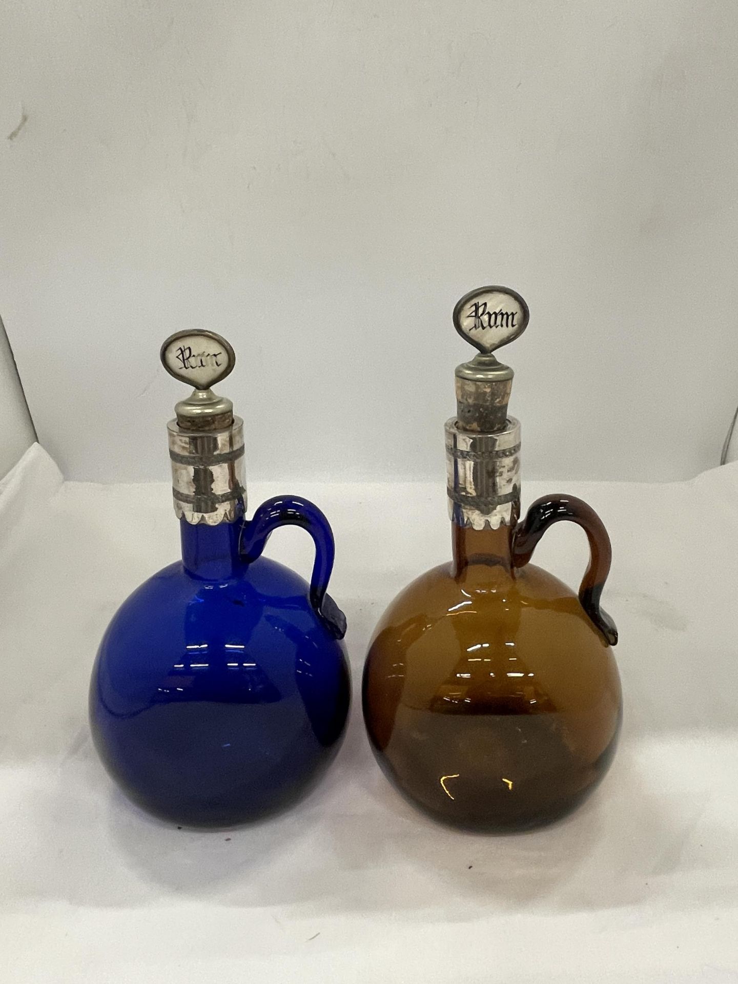 TWO ANTIQUE COLOURED GLASS DECANTERS/FLAGONS WITH SILVER PLATED COLLARS, PORT AND RUM CORKS