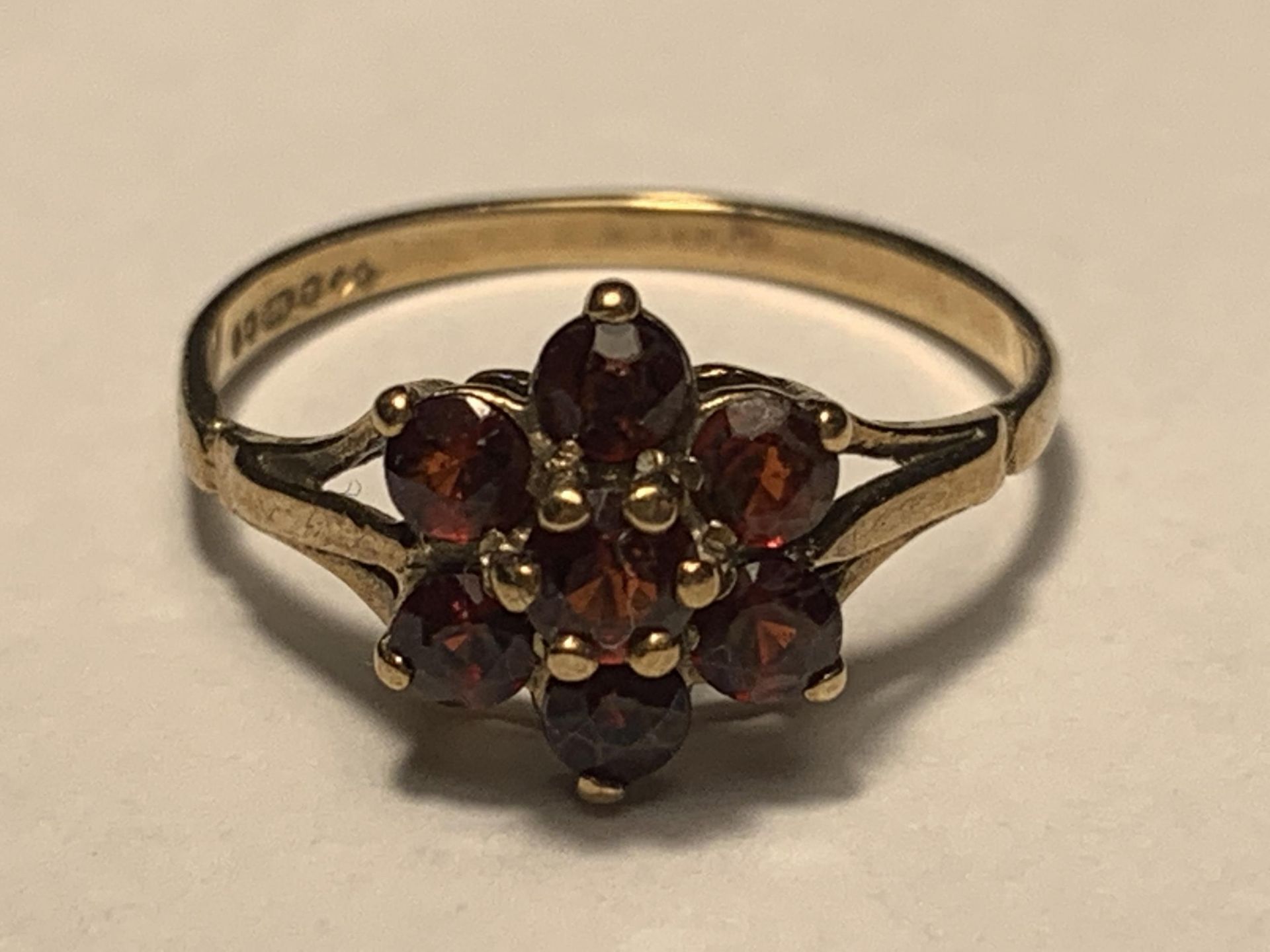 A 9 CARAT GOLD RING WITH SEVEN GARNETS IN A FLOWER DESIGN SIZE M