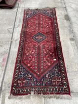 A SMALL RED PATTERNED FRINGED RUG