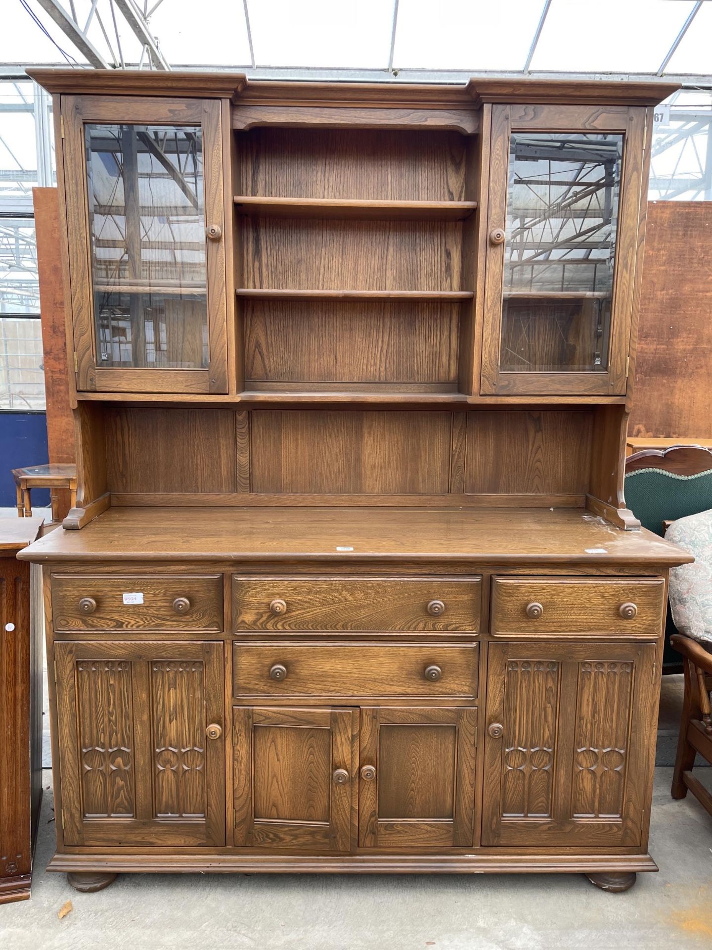 AN ERCOL ELM DRESSER WITH FOUR DRAWERS AND CUPBOARDS TO THE BASE, THE UPPER PORTION HAVING SHELVES