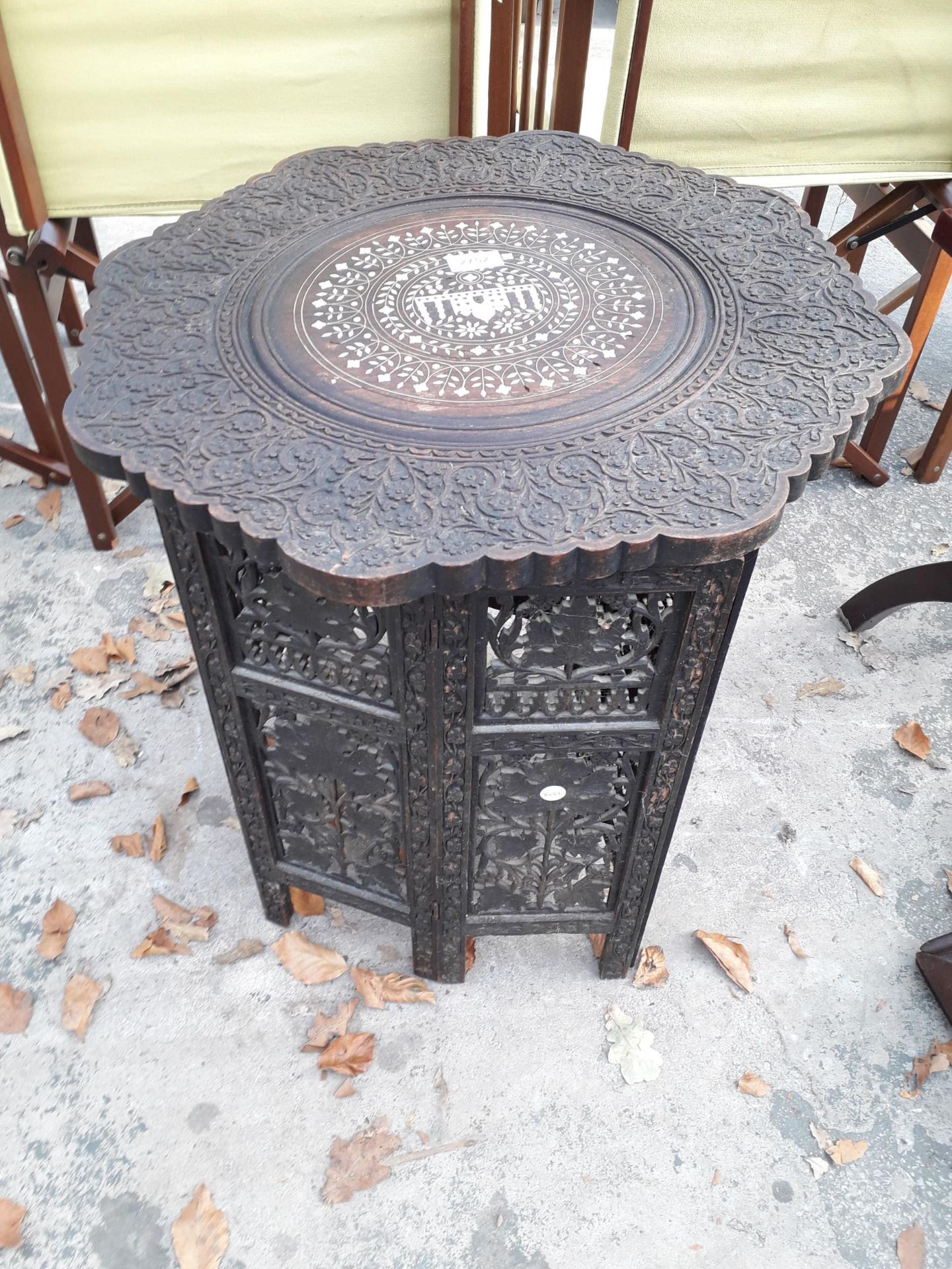 A CARVED INDIAN HARDWOOD TABLE, 22" DIAMETER, WITH FOLDING BASE, FOLIATE CARVING AND INLAY FEATURING