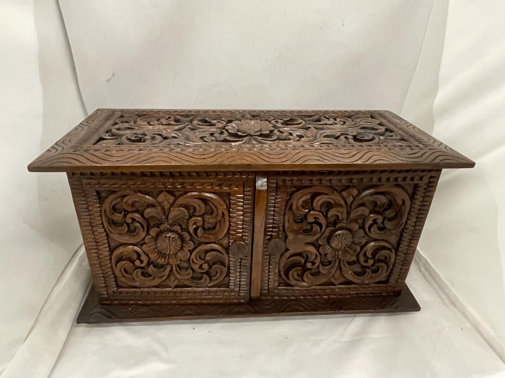 A HEAVILY CARVED JEWELLERY BOX WITH TWO DOORS REVEALING FOUR LINED DRAWERS AND A LIFT UP LID WITH