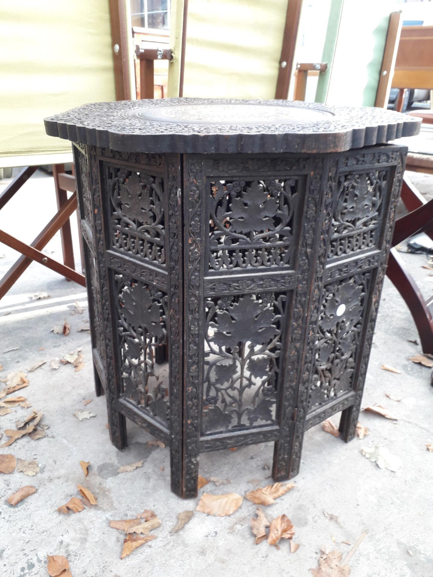 A CARVED INDIAN HARDWOOD TABLE, 22" DIAMETER, WITH FOLDING BASE, FOLIATE CARVING AND INLAY FEATURING - Image 2 of 3