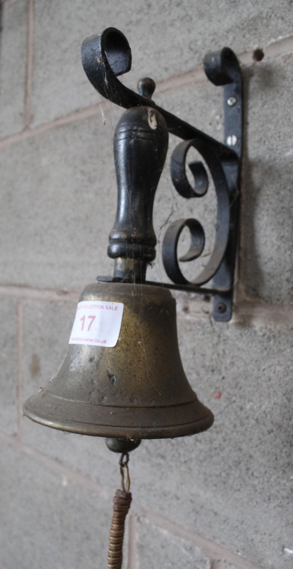 A VINTAGE BRASS BELL ON A WALL HANGING BRACKET