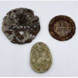 Three carved Chinese pendants/tokens, one larger hardstone example with dragon relief (6.5cm), a