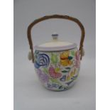 A Poole Pottery hand-decorated biscuit barrel, with finial topped cover and rattan over handle