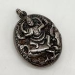 An Eastern silver locket heavily embossed with a Deity seated on an exotic bird, entwined by a
