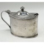 An oval hallmarked silver mustard pot with blue glass liner