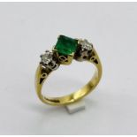 An emerald and diamond three stone ring set in 18ct gold, the central square cut emerald measuring