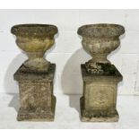 A pair of weathered Sandford Stone garden urns on plinths with floral detail to edges - overall
