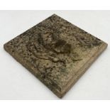 A weathered composite stone plaque with raised lion's mask detail - 29cm x 29cm