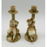 A pair of Royal Worcester candlestick figures by James Hadley of a boy and girl sitting upon a