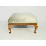 An upholstered footstool raised on cabriole legs