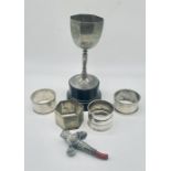 Four hallmarked silver napkin rings along with a silver trophy and silver rattle (A/F)