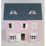 A pink wooden dolls house with a small selection of furniture