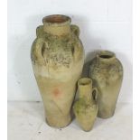 A large weathered four handled terracotta olive jar along with two similar smaller jugs. Approximate