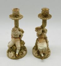 A pair of Royal Worcester candlestick figures by James Hadley of a boy and girl sitting upon a