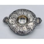 A Victorian silver strainer with shell handles and relief decoration of cherubs, tavern scene etc.