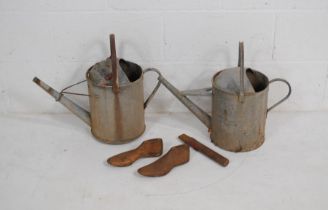 Two galvanised watering cans along with a pair of cast iron shoe lasts