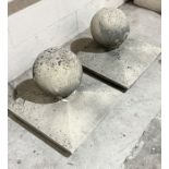 A pair of reconstituted stone gate post finials of spherical form on square plinth bases - 54cm wide