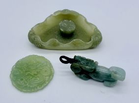 Three pieces of carved jade. A temple lion pendant, an ornately carved round pendant depicting a