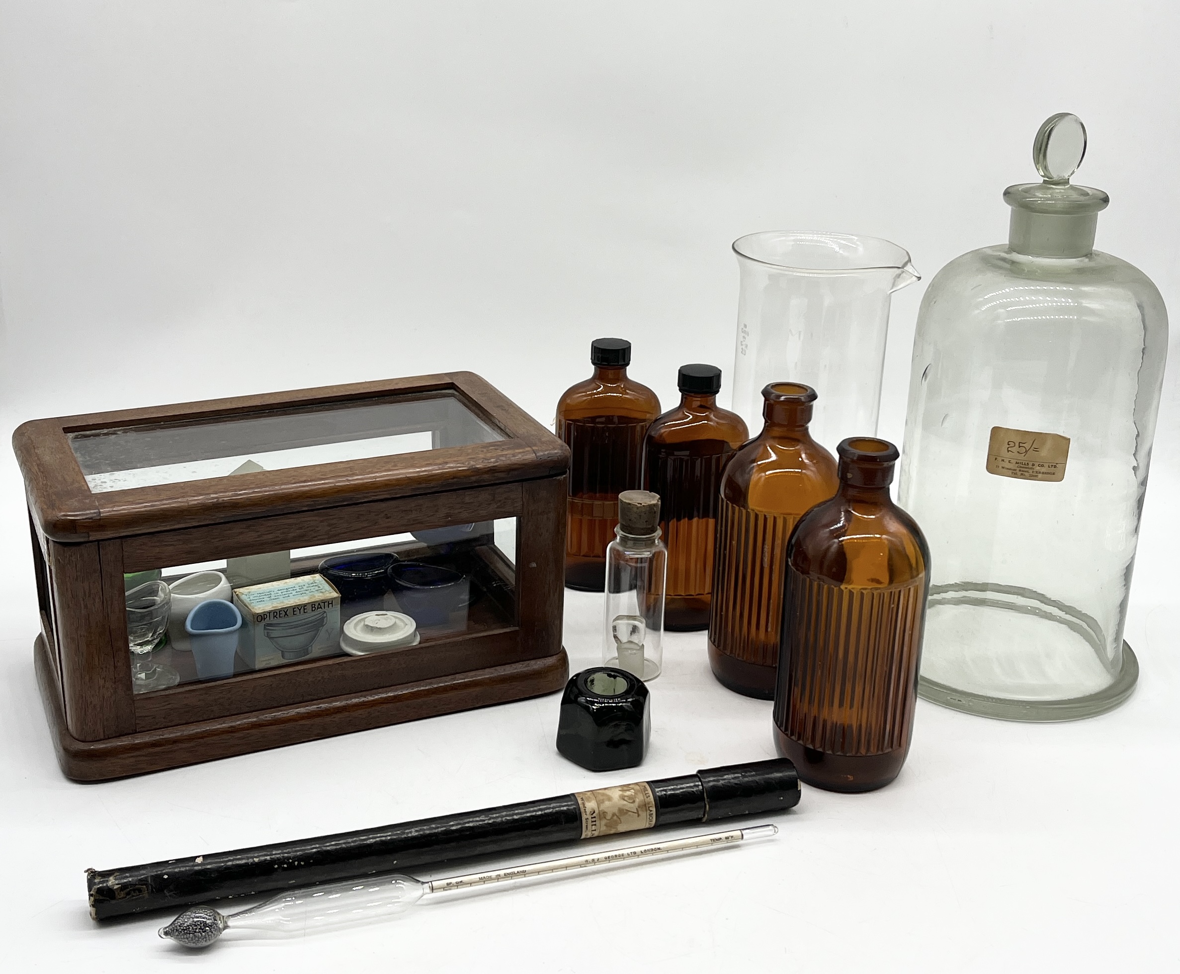 A collection of chemists bottles and bell jars along with a small wooden medical cabinet