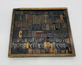 A printer's style tray containing a collection of vintage letterpress wooden printing blocks