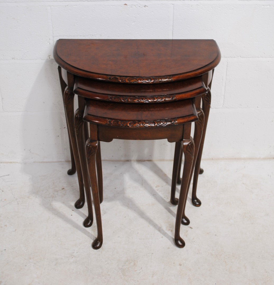 A walnut veneered nest of three demi-lune tables, with carved decoration, raised in cabriole legs