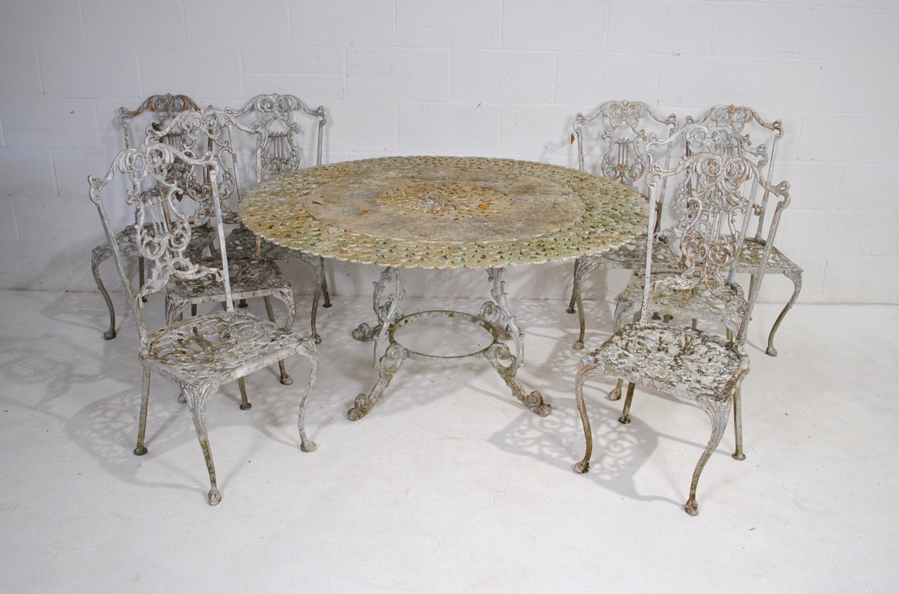 A weathered cast aluminium circular garden table with a set of eight chairs, with lyre backs - one