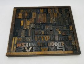 A printer's style tray containing a collection of vintage letterpress wooden printing blocks