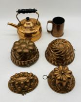 Four vintage copper jelly moulds, along with a copper tankard and kettle.
