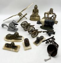 A collection of various items including brass canons, brass Buddha, cast iron doorstop in the form