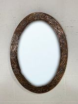 An Arts & Crafts oval copper mirror with embossed floral decoration, 68cm x 49cm