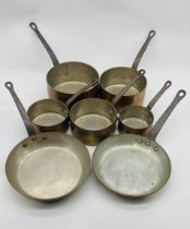 A set of five copper saucepans, along with two frying pans