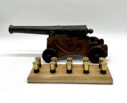 A model cannon along with ten numbered shotgun cartridges with a stand.