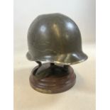 A Battle worn military helmet U.S army on turned wooden base with metal stand.